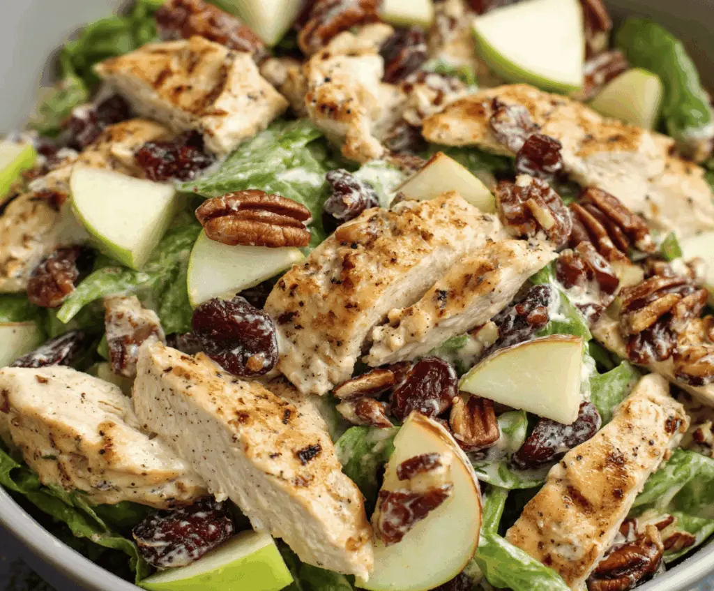 Fresh apple pecan chicken salad with chopped apples, roasted pecans, and tender chicken on a white plate, garnished with greens and drizzled with dressing