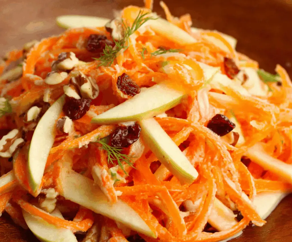 Fresh carrot and apple salad with sliced carrots and crisp apples topped with chopped nuts, served in a glass bowl for a healthy, colorful dish.