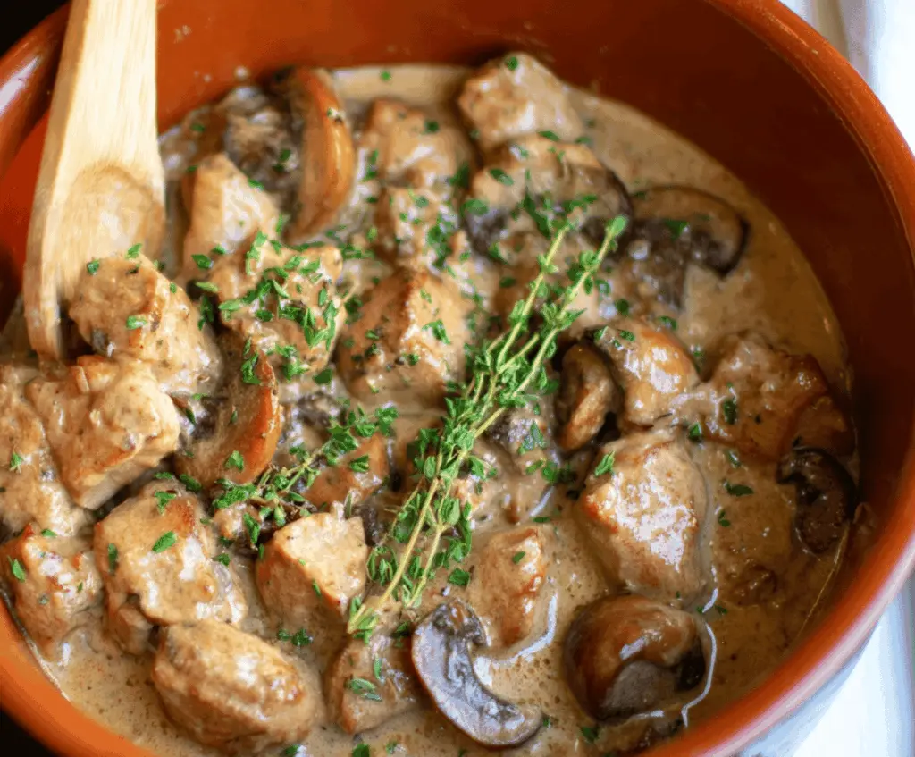 Creamy Chicken and Mushroom Stew in a bowl, garnished with fresh herbs, served alongside bread on a rustic wooden table
