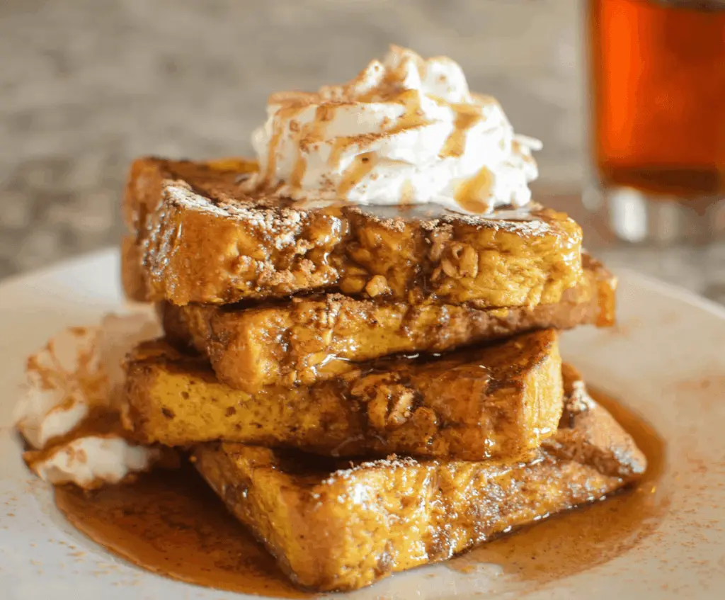 Golden Pumpkin Pie French Toast topped with whipped cream and cinnamon, served with fresh maple syrup for a delicious fall breakfast