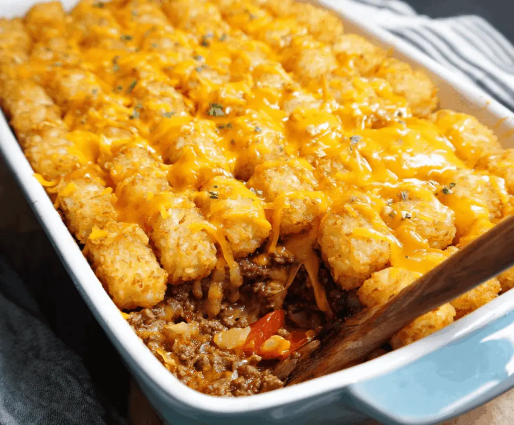 Delicious cheeseburger tater tot casserole topped with melted cheese, fresh lettuce, tomatoes, and pickles, served in a baking dish