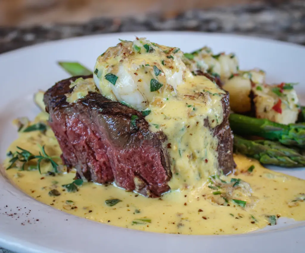 Delicious Steak Oscar topped with fresh asparagus, crab meat, and creamy Hollandaise sauce on a white plate.