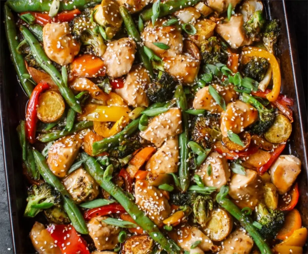 Delicious sheet pan sesame chicken with colorful vegetables on a baking tray.